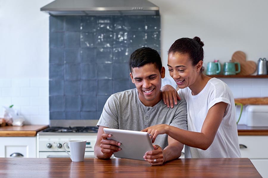 Blog - Couple Smiles as They Use a Tablet in Their High-End Kitchen, Coffee Nearby