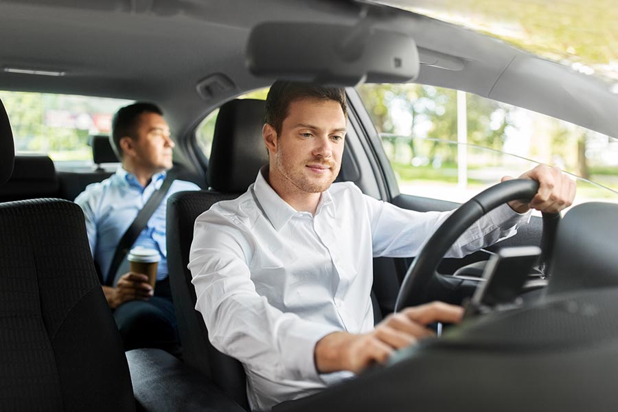 Rideshare Insurance - Professional Ride Share Driver Checks in on His Phone, a Client in the Back Seat