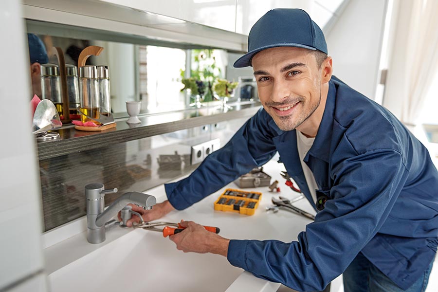 Specialized Business Insurance - Contractor Works on a Faucet Installation in a Home Wearing Blue Uniform