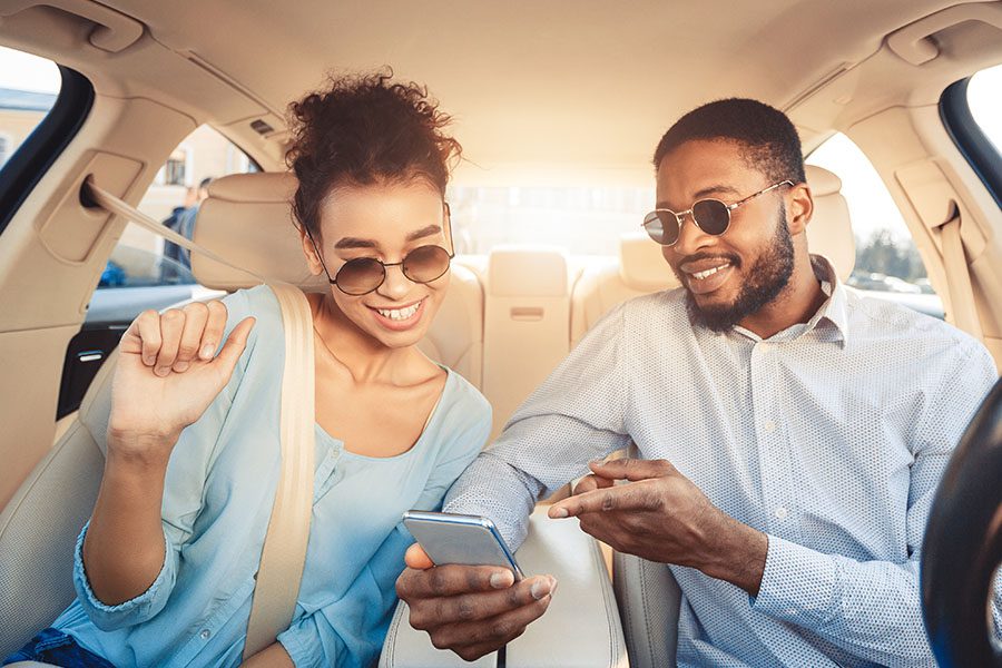Auto Quote - Man Parked Showing a Woman in the Passenger Seat Something on His Phone While They Sit in a Car
